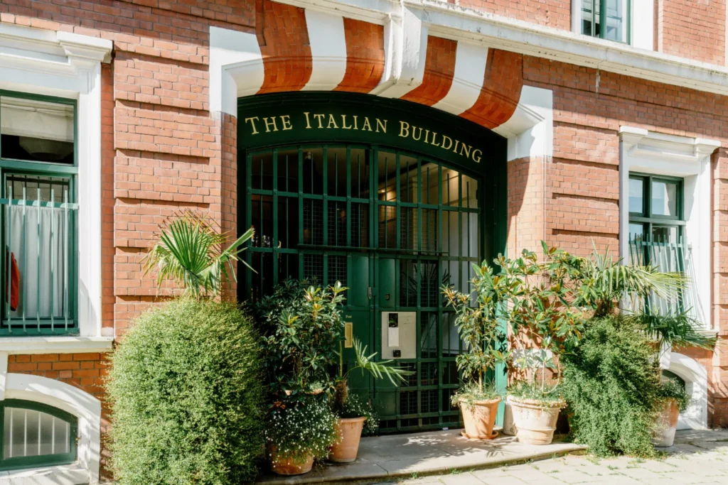 A green gated building front with gold writing above the door reading 'The Italian Building' and plants surround the entrance.